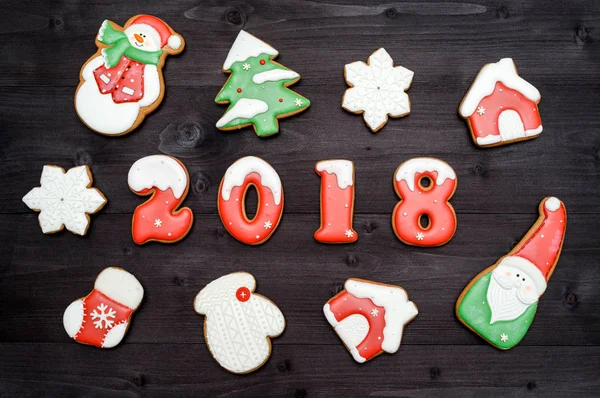 Šťastný nový rok 2018 znaménko symbol a červené a bílé perníčky na tmavé dřevěné pozadí. Pohled shora, ploché ležel. Vánoční cukroví, santa, sněhulák, vločka, dům, vánoční ponožku, volné místo — Stock fotografie