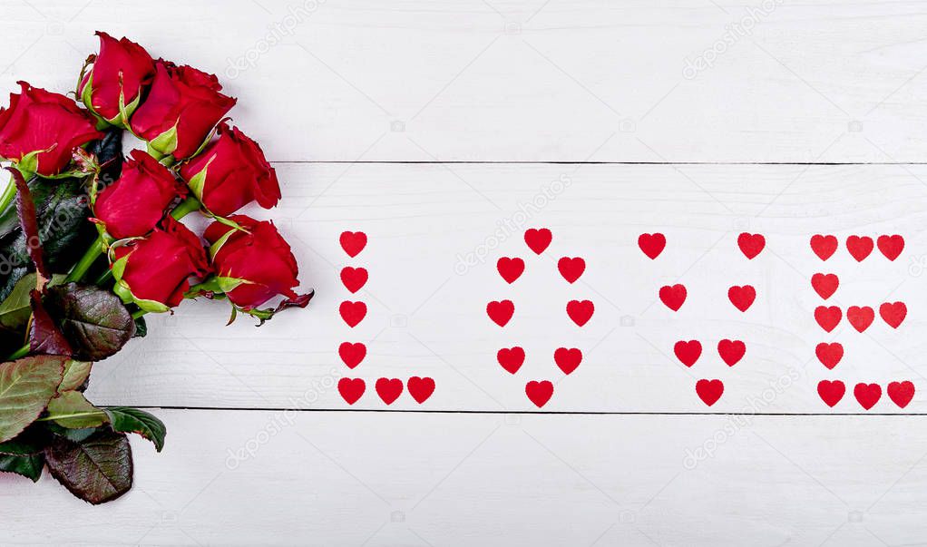 Bouquet of red roses and sign love made from paper hearts on white background, copy space. Greeting card for Valentines Day, Womans Day, Mothers Day. Love, wedding concept, flat lay, top view 