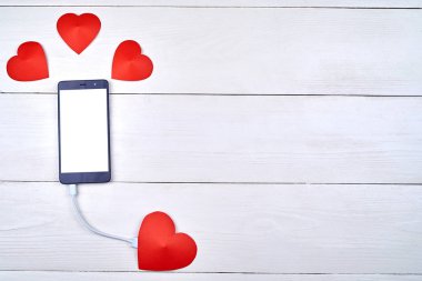 Mobil akıllı telefon ile kopya alanı beyaz ahşap arka plan üzerinde kırmızı kağıt kalp ile şarj beyaz boş perde. Sevgililer günü için mockup şablonu. Aşk, teknoloji kavramı. Üstten görünüm, düz yatıyordu