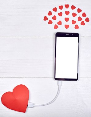 Mobil akıllı telefon ile kopya alanı beyaz ahşap arka plan üzerinde kırmızı kağıt kalp ile şarj beyaz boş perde. Sevgililer günü için mockup şablonu. Aşk, teknoloji kavramı. Üstten görünüm, düz yatıyordu