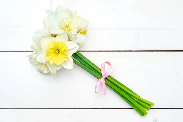 Bouquet of daffodil flowers with pink ribbon on white wooden background, copy space. Top view, flat lay. White narcissus. Spring flowers. Greeting card for March 8 (Women\'s Day), Mother\'s day. Easter