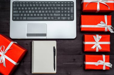 Ahşap masa, kopya alanı üzerinde üstten görünüm açık dizüstü bilgisayar, boş defter ve kırmızı hediye kutuları. Düz yatıyordu. Online alışveriş, tatil satış. Sevgililer günü, Bayan günü, anneler günü, Doğum günü için hediye
