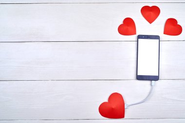 Mobil akıllı telefon ile kopya alanı beyaz ahşap arka plan üzerinde kırmızı kağıt kalp ile şarj beyaz boş perde. Sevgililer günü için mockup şablonu. Aşk, teknoloji kavramı. Üstten görünüm, düz yatıyordu