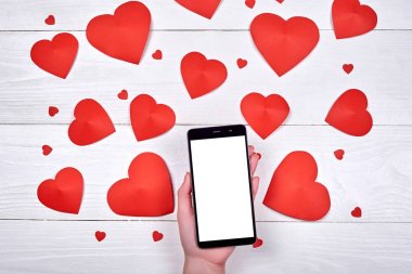 Mobil akıllı telefon app sunu el ve ahşap zemin, kopya alanı üzerine kırmızı kağıt kalpler için boş beyaz ekran ile kapatın. Düz yatıyordu, en iyi görünüm. Sevgililer uygulama şablonu 