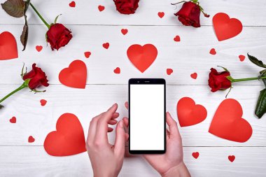 Kadın el, kırmızı Kağıt kalpleri ve ahşap zemin, kopya alanı üzerine gül çiçek beyaz boş ekran ile mobil akıllı telefon yakın çekim. Düz yatıyordu, en iyi görünüm. Sevgililer günü uygulama mockup şablonu