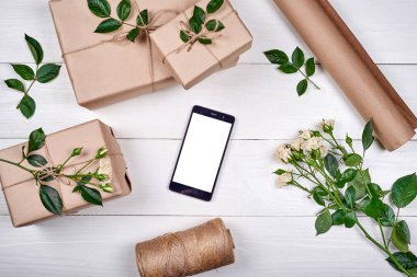 Kraft taze gül ve ahşap zemin, kopya alanı üzerine beyaz ekran ile hareket eden smartphone hediye kutuları sarılı. Tebrik kartı mockup. Üstten görünüm, düz yatıyordu. Bahar, anneler günü, Womans gün