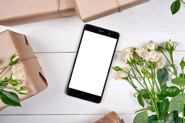 Kraft taze gül ve ahşap zemin, kopya alanı üzerine beyaz ekran ile hareket eden smartphone hediye kutuları sarılı. Tebrik kartı mockup. Üstten görünüm, düz yatıyordu. Mobil uygulaması tanıtımı
