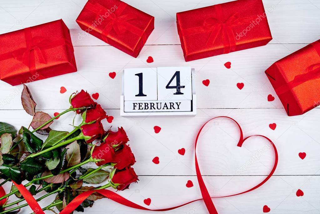 Valentines Day background with bunch of red roses, gift boxes, ribbon shaped as heart and wooden block calendar february 14 , copy space. Greeting card mockup. Love concept. Top view, flat lay