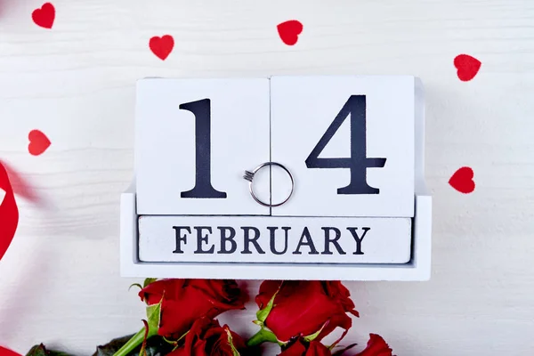 Primer plano del anillo de diamantes en el calendario de bloques de madera 14 de febrero en la mesa blanca con corazones de papel y rosas. Fondo del Día de San Valentín. Amor, compromiso, concepto de vacaciones. Piso tendido, vista superior —  Fotos de Stock