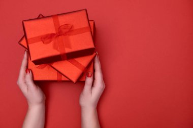 Kırmızı arka planda kırmızı hediye kutularını tutan kadınların ellerini kapatın.