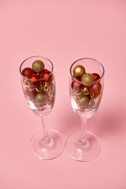 Pastel pembe arka planda altın ve kırmızı süslemeli şampanya kadehleri.