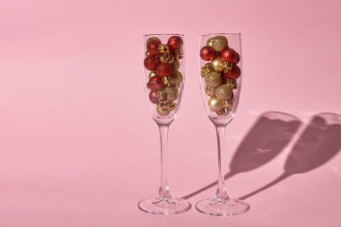Pastel pembe arka planda altın ve kırmızı süslemeli şampanya kadehleri.
