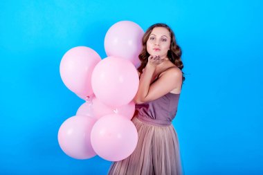 Pembe helyum balonlu mutlu genç kadın mavi arka planda bir öpücük savuruyor.