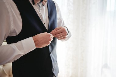 Beyaz gömlekli bir adam. Kapalı odada yelek ilikliyor. Yaklaş.