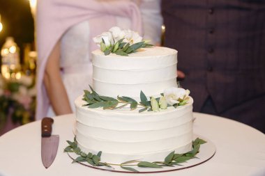 Restoranda çiçekler ve yeşil yapraklarla süslenmiş zarif beyaz düğün pastası.