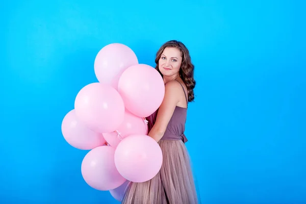 Hermosa mujer joven en vestido que se divierte con globos de helio rosa sobre fondo azul — Foto de Stock