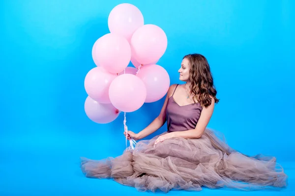 Retrato de larga duración de la joven feliz en vestido con globos de aire rosa sobre fondo azul — Foto de Stock