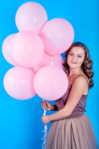 Feliz joven sonriente en vestido sosteniendo globos de helio rosa sobre fondo azul — Foto de Stock