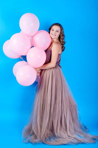 Retrato de larga duración de una joven alegre en vestido con globos rosados sobre fondo azul — Foto de Stock