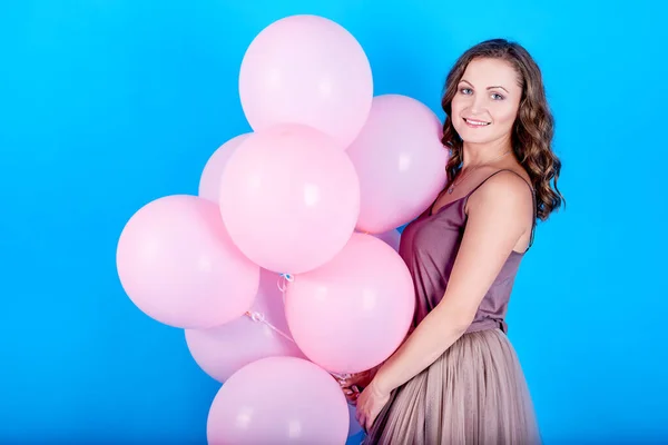 Feliz joven sonriente en vestido sosteniendo globos de aire rosa sobre fondo azul — Foto de Stock