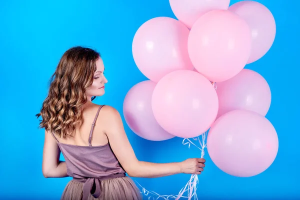 Hermosa joven en vestido sosteniendo globos rosados sobre fondo azul — Foto de Stock