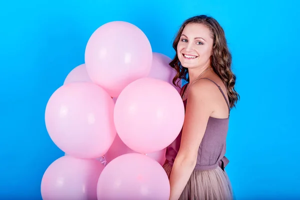 Hermosa mujer joven en vestido sosteniendo globos de aire rosa sobre fondo azul — Foto de Stock