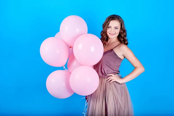 Feliz joven sonriente en vestido sosteniendo globos de aire rosa sobre fondo azul — Foto de Stock
