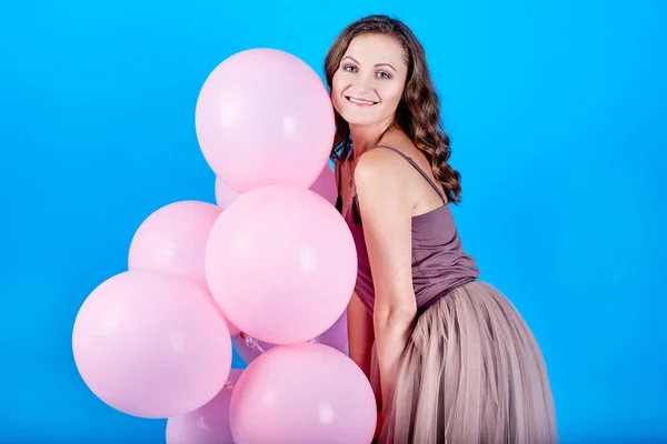 Mujer joven feliz en vestido sosteniendo globos de aire rosa sobre fondo azul — Foto de Stock