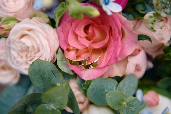 Primo piano di due fedi nuziali d'oro su bouquet da sposa di rosa a — Foto Stock