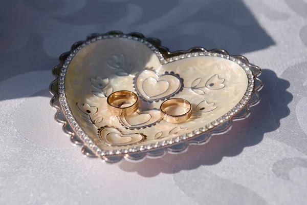 Two golden wedding rings on plate shaped as heart on white table — Stock Photo, Image