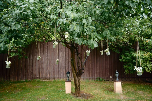 Decoraciones de boda rústicas con flores en tarro de vidrio colgado en el árbol verde al aire libre —  Fotos de Stock