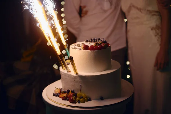 뒤쪽에는 신부와 신랑 이 있는 싱싱 한 열매 로장식된 우아 한 흰 웨딩 케이크 — 스톡 사진