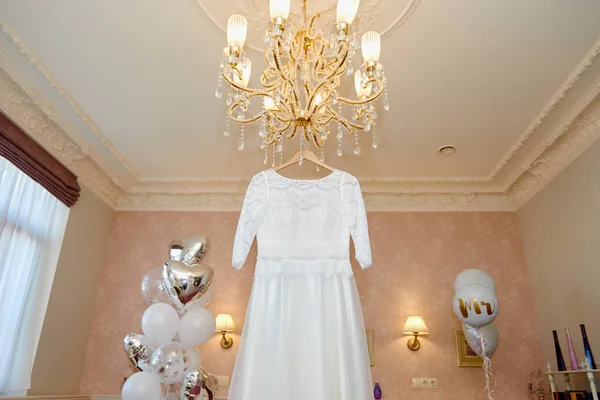 Vacker bröllopsklänning hängande på hängare på lyx ljuskrona i hotellrum — Stockfoto