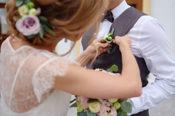 Närbild av bruden sätta på boutonniere till brudgummen väst — Stockfoto