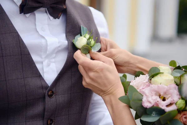 Närbild av bruden sätta på boutonniere till brudgummen väst — Stockfoto