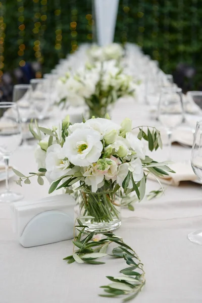 户外餐馆婚宴桌上玻璃花瓶中的白花绿叶布置得很漂亮 — 图库照片