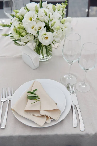 Table setting with beige napkin on empty white plate, wineglasses and cutlery on table at wedding reception