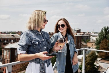 Mutlu gülümseyen bayan arkadaşlar bira içip cep telefonlarını çatıda ya da barda kullanıyorlar.