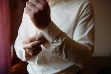 Lüks beyaz gömlek kolunun düğmelerini ilikleyen adam, kopyalama alanı. Damat pencerenin yanında duran kol düğmelerini düzeltir