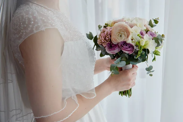 Portrait de belle mariée en robe de mariée debout avec bouquet nuptial près de la fenêtre dans la chambre, espace de copie. Préparation matinale de la mariée — Photo