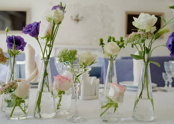 Цветочное оформление свадебного стола в ресторане, пространство для копирования. Аромат розовых роз, фиолетовой эустомы и зелени в стеклянных вазах — стоковое фото
