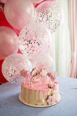 Round pink birthday cake decorated with lollipops, gingerbreads, flowers, beads number two on the top