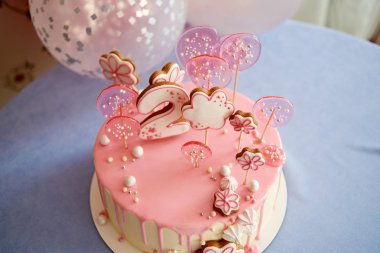 Round pink birthday cake decorated with lollipops, gingerbreads, flowers, beads number two on the top
