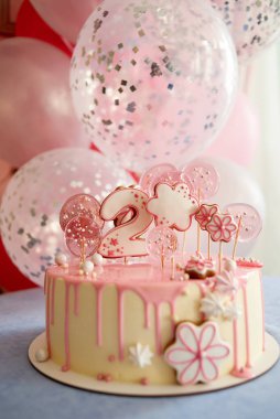 Round pink birthday cake decorated with lollipops, gingerbreads, flowers, beads number two on the top