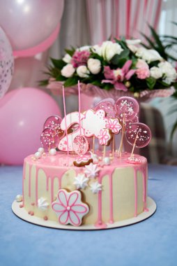 Round pink birthday cake decorated with lollipops, gingerbreads, flowers, beads number two on the top