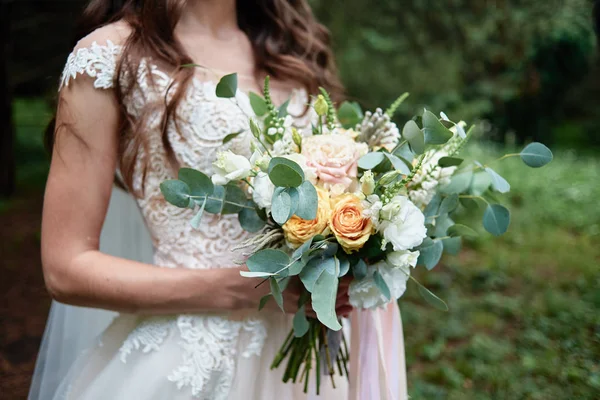 Прекрасный свадебный букет из бежевых роз и зелени в руках невесты на открытом воздухе — стоковое фото