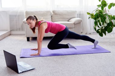 Güzel genç bir kadın evdeki oturma odasında kalas egzersizi yapıyor.