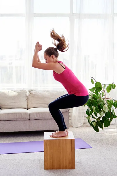 Young woman doing box jump exercise in living room at home, copy