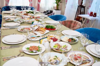 Masa beyaz tabaklar, peçeteler, çatal bıçak takımı ve şarap kadehleriyle hazır.