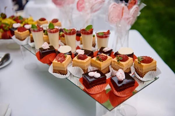 キャンディーバーには、イチゴとチョコレートケーキのスライス、屋外のテーブルの上のガラスのクリームデザート、コピースペースがあります。誕生日パーティーや結婚式のレセプションのためのデザートテーブル。休日のコンセプト — ストック写真